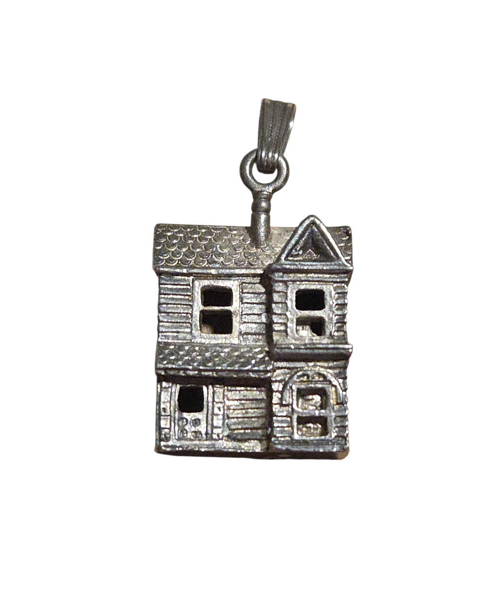 Front of silver-tone dollhouse pendant with textured roof, windows, and door