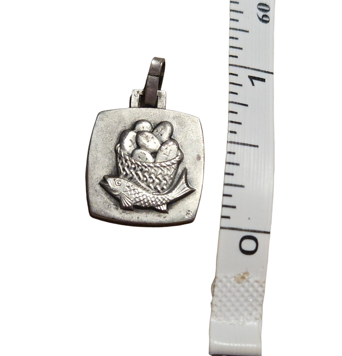Vintage fish and loaves pendant photographed beside ruler